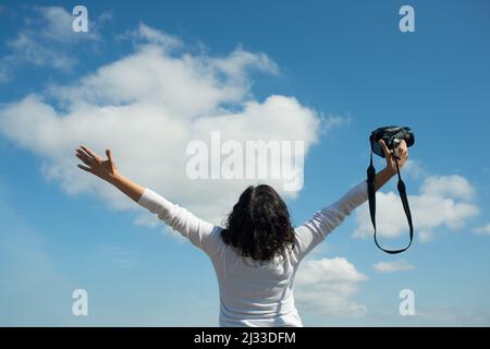 Woman photographer excited about career possibilities. Happy woman photographer with arms extended and camera in one hand. Stock Photo