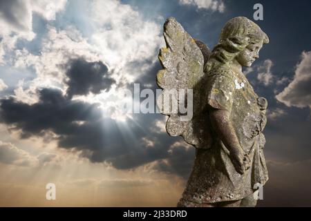 Stone statue of winged angel against rays of sunlight behind clouds Stock Photo