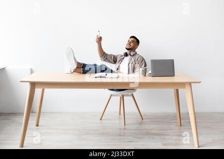 Young Arab man switching on air conditioning at home office Stock Photo