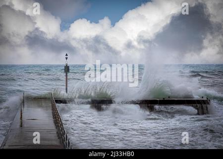 Stormy ocean waves splashing over a pier during a winters storm Stock Photo