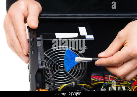 Service center employee using a small brush to clean dust off the grid of the power unit of a personal computer. Stock Photo