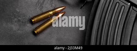 Two bullets and Kalashnikov assault rifle on gray concrete background banner, top view panoramic web header. Cartridge 7.62 caliber for ak 47. Wide sc Stock Photo