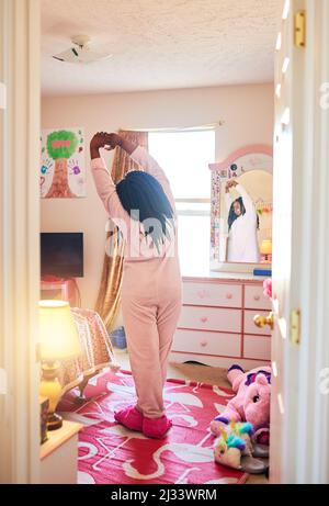 When she wakes up, she likes to stretch. Rearview shot of an unrecognizable little girl stretching in her bedroom. Stock Photo