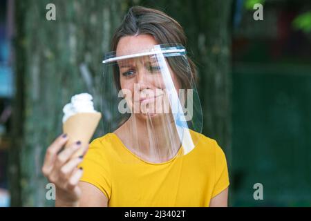 young woman with face visor holding an ice cream in hand Stock Photo