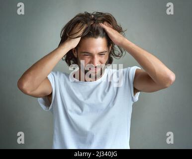 This is so frustrating. Studio shot of a young man looking upset against a grey background. Stock Photo