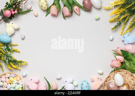 Easter concept. Frame of eggs in a basket, flowering branches of toy rabbits on a gray background. Stock Photo