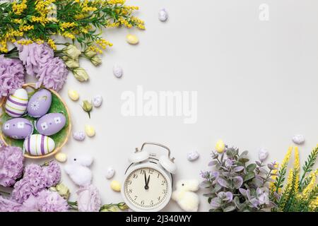Easter concept. Purple flowers and blooming yellow sprigs of eggs in a basket with an alarm clock on a gray background. Stock Photo