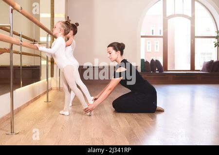 Female dance instructor trying to comfort one of her little students during a ballet class. Girls are engaged in choreography in the ballet school.You Stock Photo