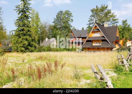 Zakopane, Poland - September 12, 2016: Behind an undeveloped meadow you can see houses built in the style of a highlander cottage. These houses are su Stock Photo