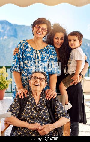 Four generations living together. Portrait of a cheerful family standing and holding each other while looking into the camera outside at home. Stock Photo