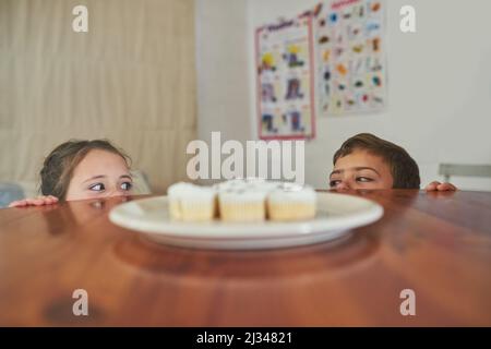 I spy with my little eye.... Cropped shot of two naughty children eyeing a plate of cupcakes. Stock Photo