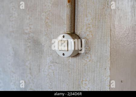 Old round light switch on a wall with a cable. Retro toggle switch in an East German apartment. Interior design of the past in a bad dirty condition. Stock Photo
