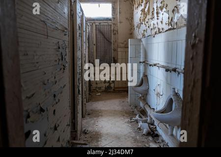 Row of old toilets in the bathroom of an abandoned public building. Paint is peeling off the walls. Dirty urinals are in the room with a lot of dust. Stock Photo