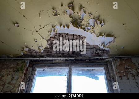 Damaged ceiling on top of a window. Eroded building structure and paint peeling off. Weathered interior of a room. Cracks in the wall of an old house. Stock Photo