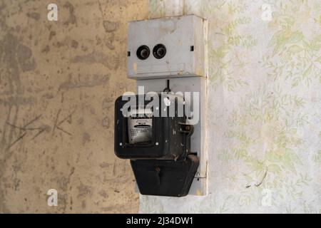 Old electric meter on a wall in an abandoned building. Electrical equipment to measure power consumption for accounting. Old vintage wallpaper. Stock Photo