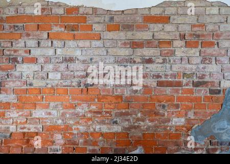 Old red brick wall background texture with broken plaster parts on it. Dirty and dusty surface of a rough building exterior. Pattern of small bricks. Stock Photo