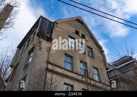 Abandoned building with a damaged facade and a broken window. Looking up on an empty old house with the blue sky in the background. Lost place ruin. Stock Photo
