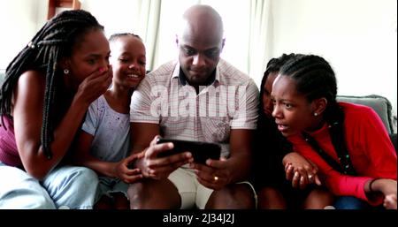 Family reaction in shock emotion looking at cellphone device news. African kids and parents reacting to surprise Stock Photo