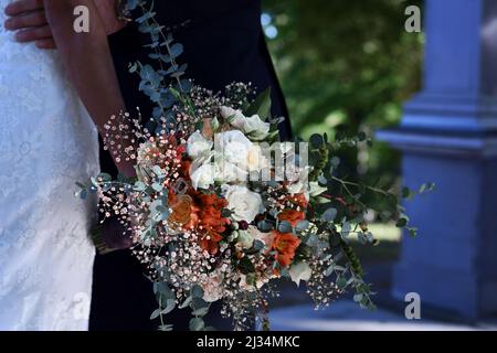 Beautiful wedding bouquet that is being hold by the bride. Unrecognizable bride and groom in the background. Photo taken outdoors. Stock Photo