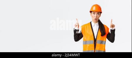 Building, construction and industrial concept. Surprised and curious asian female construction manager, engineer in safety helmet and reflective Stock Photo