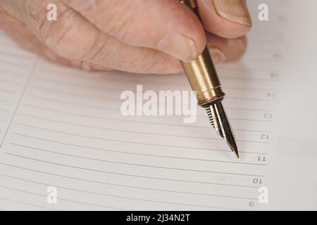 Gold coloured fountain ink pen in senior woman hand about to write something on empty daily planner page, closeup detail Stock Photo