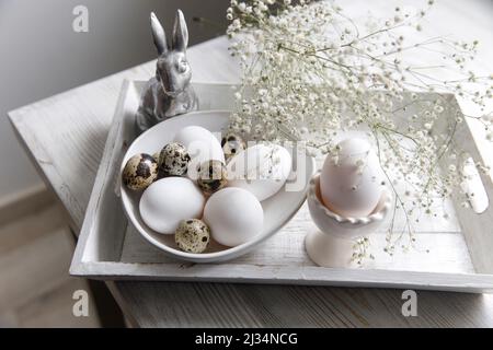 Table decorated for Easter in beige tones. Dried gypsophila, chicken and quail eggs, a silver figurine of a hare and a cup of coffee. Easter concept. Stock Photo