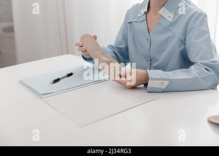 Doctor holding an insole while sitting at a table. Orthopedist tests the medical device. Orthopedic insoles. Foot care. Flat Feet Correction Stock Photo