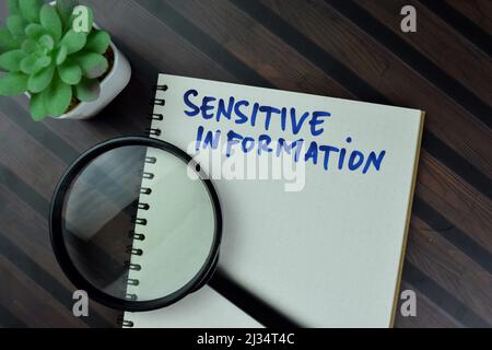 Sensitive Information write on a book isolated on Wooden Table. Stock Photo