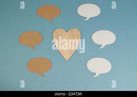 Oval speech bubbles against blue background surrounding wooden heart Stock Photo