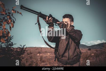 Hunter with shotgun gun on hunt. Calibers of hunting rifles. Hunter with Powerful Rifle with Scope Spotting Animals. Poacher in the Forest. Stock Photo