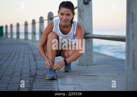 Lacing up before my run. Shot of a sporty young woman tying her shoelaces while out for a run. Stock Photo