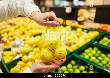 Hand of a customer at the fruit and vegetable stand in the supermarket with a bag of lemons Stock Photo