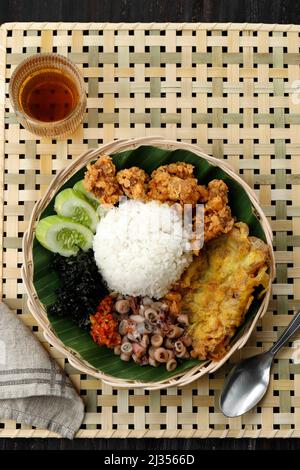 Top View Nasi Campur Cumi Asin, White Rice with Sautee Salted Squid, Sambal, Egg, Kulit Ayam Crispy Chicken Skin, and Boiled Cassava Leaf. Stock Photo