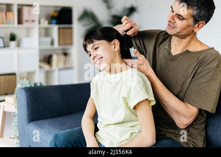 Caring father brushing his daughter hair at home. Stock Photo