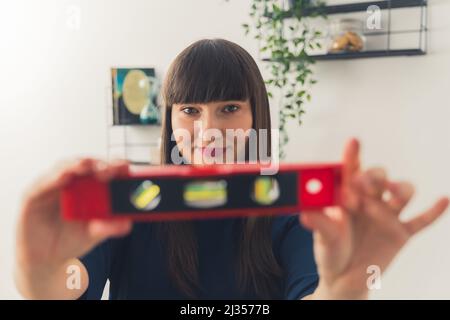 Caucasian brown-haired woman looking at camera while holding a sprit level. Indoor shot. High quality photo Stock Photo