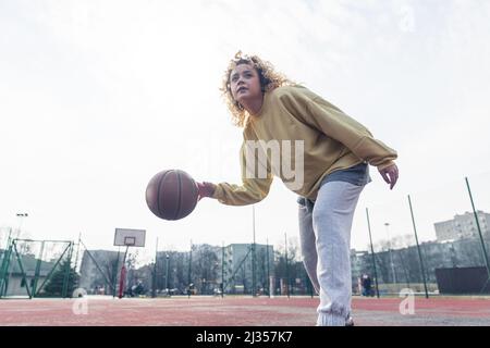 Young blond Caucasian woman plays basketball in baggy clothes, looking up copy space medium full shot . High quality photo Stock Photo