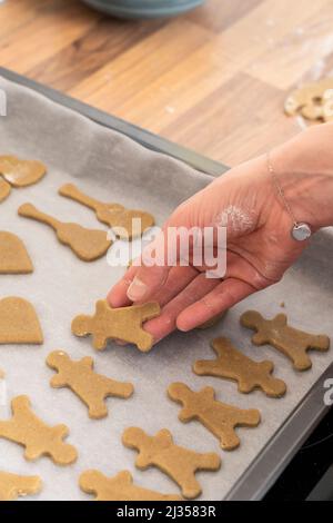 A woman's hand laying out gingerbread me on a baking tray for baking in the oven during Christmas. England. Theme: adult hobbies, home baking Stock Photo