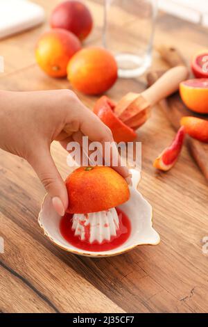 Woman squeezing ripe orange for juice on wooden table, closeup Stock Photo