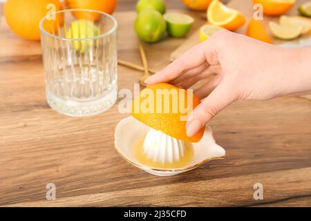 Woman squeezing orange for juice on wooden table, closeup Stock Photo