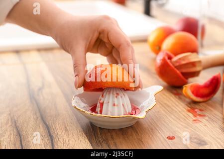 Woman squeezing orange for juice on wooden table, closeup Stock Photo