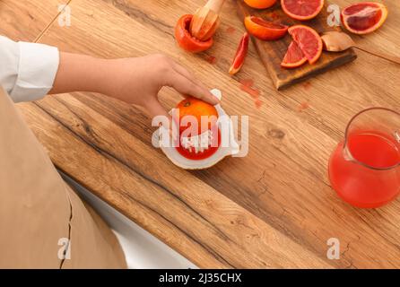 Woman squeezing ripe orange for juice on wooden table Stock Photo