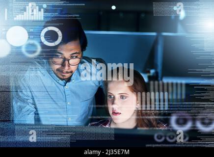 Teamwork goes a long way in the company. Shot of two focussed young programmers working together on a computer in the office at work during the night. Stock Photo