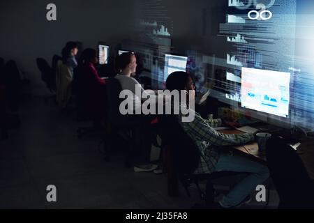 Chasing down their deadline. Rear view shot of a team of programmers coding through the night. Stock Photo