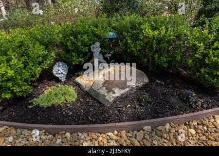 Small home garden feature with a large rock, ground cover and a boxwood hedge. Stock Photo