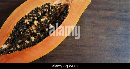 Half of a formosa papaya with seeds on a brown table half of the papaya is in the upper left corner of the picture Stock Photo