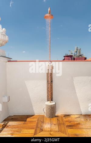 copper shower releasing water on a summer day on a terrace with wooden floors Stock Photo
