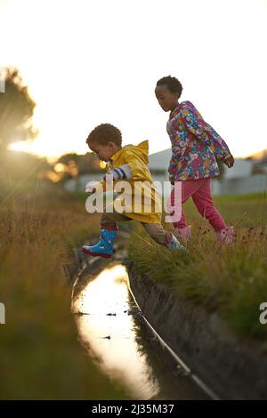 Showing sis how its done. Shot of a brother and sister jumping over water while playing outside. Stock Photo