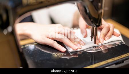 Female hand using vintage sewing machine scribbling fabric and repairing the cloth at home. Stock Photo