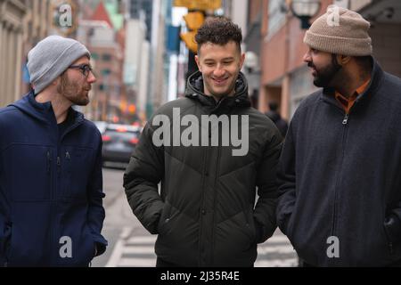 Group of interracial adult male friends talking and smiling together having conversation in the streets of downtown Toronto, Ontario Canada Stock Photo