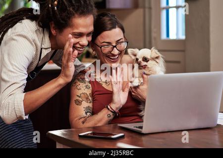 Its been so long since weve seen you. Cropped shot of a cheerful young couple having a video call while waving at the camera and holding their dog at Stock Photo